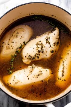 three pieces of chicken are in a pot of broth with some herbs on top