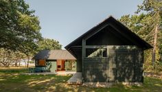 a small cabin in the middle of a field with grass and trees around it, next to a picnic table