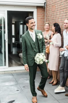 a man in a green suit and white flowers is walking down the street with other people