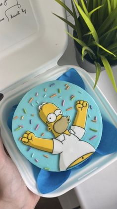 a person holding a cake with the simpsons character on it and sprinkles