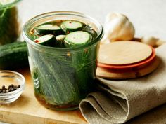 cucumbers and spices sit in a jar on a cutting board