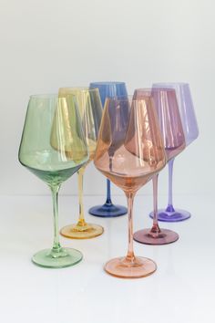 five different colored wine glasses lined up in a row on a white surface with one empty