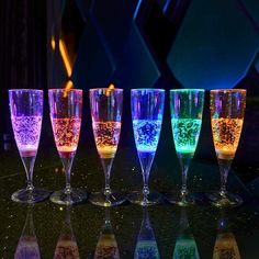 five wine glasses with different colored liquids in them sitting on a black table next to each other