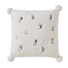 a white pillow with skiers and trees embroidered on the front, along with pom - poms