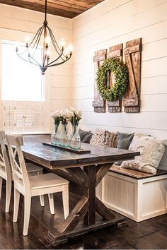 a dining room table and bench with flowers in vases on the end, surrounded by white chairs