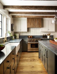 a large kitchen with wooden floors and white cupboards, stainless steel appliances and wood beams