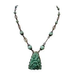 a necklace with a green stone buddha head and beads hanging from it's sides