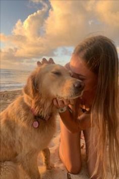 a woman is kissing her dog on the beach at sunset with clouds in the background