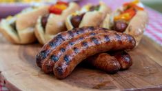 two hot dogs and three sausages on a cutting board with a checkered tablecloth