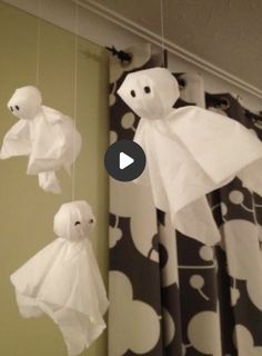 paper ghost decorations hanging from the ceiling in front of a window with black and white curtains