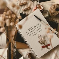 an open notebook sitting on top of a pile of books next to some dried flowers