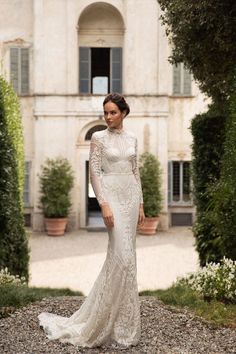 a woman standing in front of a building wearing a white wedding dress with long sleeves