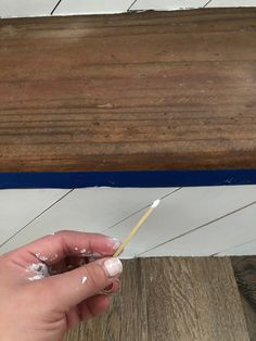 a person is holding a toothbrush in their left hand and painting the wood with white paint