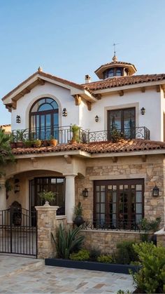 a large white house with lots of windows and plants on the front porch, surrounded by greenery