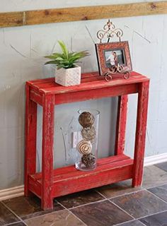 a red wooden table with an empty vase and small potted plant sitting on top