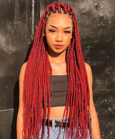 a woman with long red dreadlocks standing in front of a black wall and looking at the camera