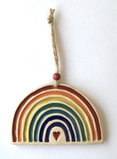 a wooden rainbow ornament hanging on a string with a heart in the center