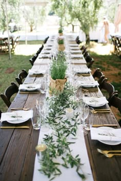 a long table set with place settings and greenery on it for an outdoor event