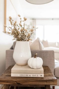 a white vase sitting on top of a wooden table next to a book and plant