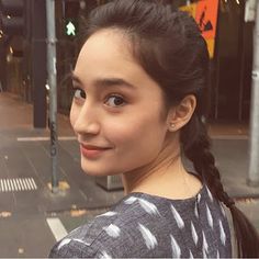 a young woman standing on the street with her hair in a pony tail style braid