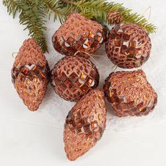 some brown glass beads are next to a pine branch on a white surface with gold sequins