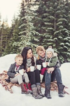 a group of people sitting on top of a blanket in the snow with coffee cups