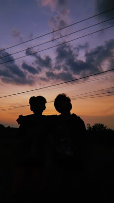 two people standing next to each other in front of power lines at sunset or dawn