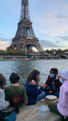 four children sitting on the edge of a river in front of the eiffel tower