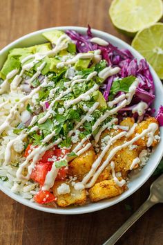 a white bowl filled with salad next to a fork and lime wedges on the side