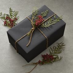 a black gift box tied with twine and surrounded by greenery on the floor