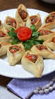 a white plate topped with pastries covered in meat and veggies next to silverware