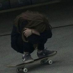 a skateboarder crouches down on the ground with his head in his hands