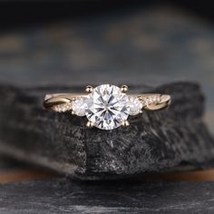 an engagement ring with three stones in the center on top of a stone slab next to a rock