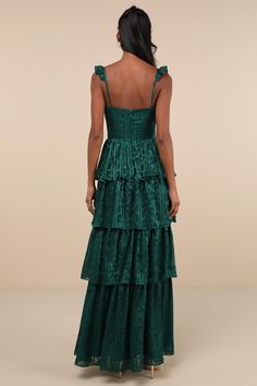 a woman wearing a green dress with tiered skirt and open back, looking down at the