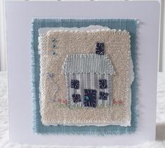 an embroidered card with a house on the front and blue trimmings around it