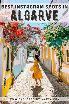 a woman walking down a cobblestone street with red flowers on the trees and buildings in the background