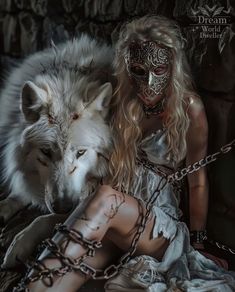 a woman sitting next to a wolf with chains around her ankles and wearing a mask