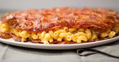 a white plate topped with macaroni and cheese covered in bacon on top of a table