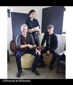 three men are sitting in a room with guitars