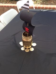 a pirate ship in a jar on top of a black table cloth with white chairs around it