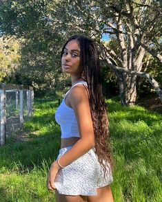 a young woman standing in the grass with her long hair pulled back and wearing shorts