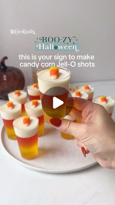 a person holding a glass filled with candy corn jello shots on top of a white plate