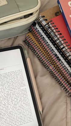 an open book sitting on top of a bed next to notebooks