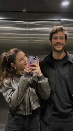 a man and woman taking a selfie in front of an elevator door with their cell phone