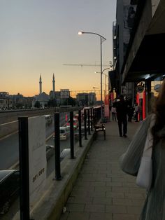 people are walking down the sidewalk next to a bus stop at sunset or dawn in an urban setting