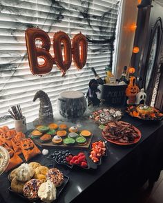 a table topped with lots of halloween treats and balloons that spell boo on top of it