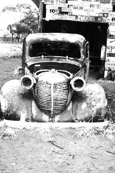 an old car is parked in front of a building with signs on the side of it