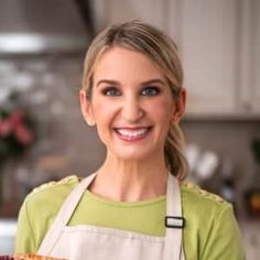 a woman in an apron is holding a plate of food and smiling at the camera