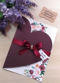 a heart shaped card with a red ribbon on it next to purple flowers and a tag