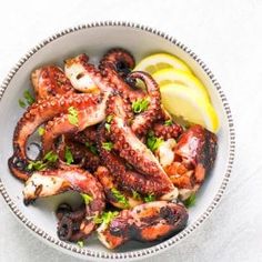 an octopus dish with lemon wedges and parsley in a bowl on a white surface